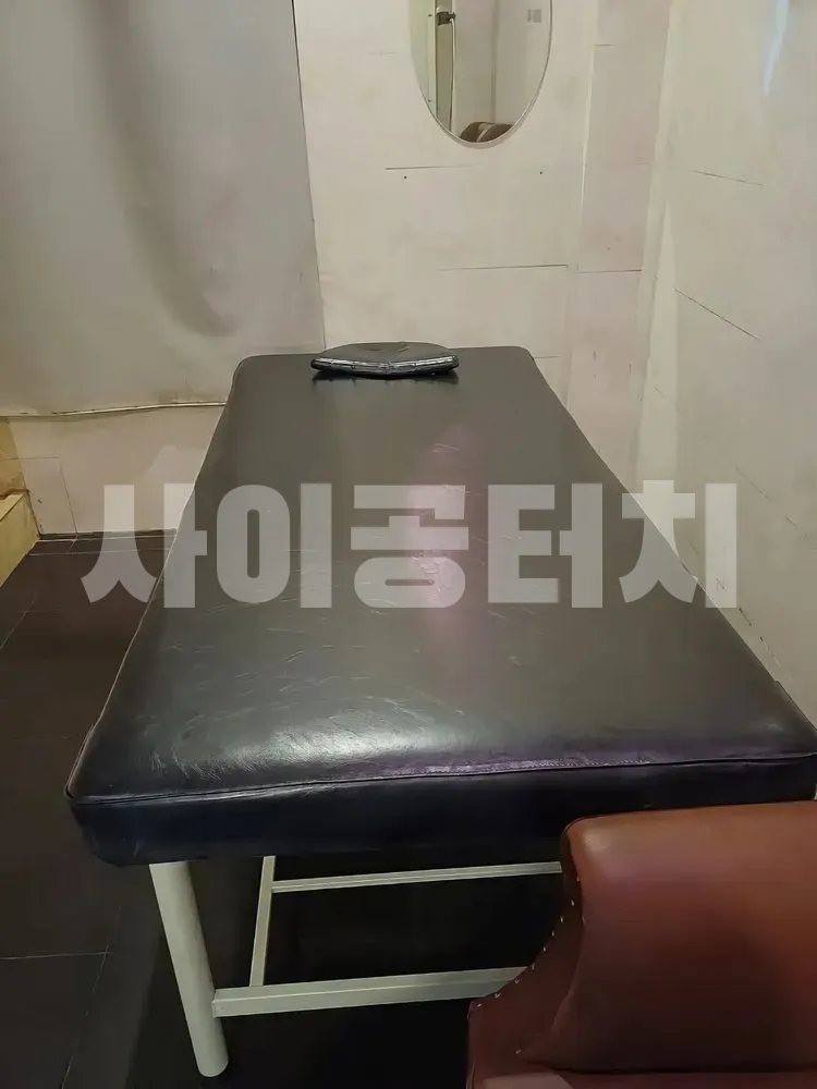 흰색 타일 벽 앞의 검은색 마사지 베드